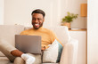 © Prostock-studio - Cheerful Black Man Using Laptop Sitting On Couch At Home
