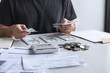 © Ngampol - Images of stacking coin pile and Husband using calculator to calculating expenditure receipt bills of various activity cost and expenses in home office and written make report to plan of spent