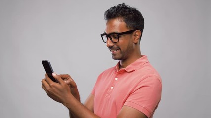 Poster - technology, internet, communication and people concept - happy indian man in glasses using smartphone over grey background