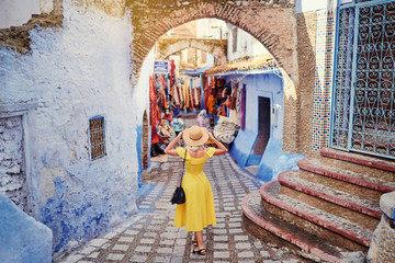 Wall Mural - Colorful traveling by Morocco. Young woman in yellow dress walking in  medina of  blue city Chefchaouen.