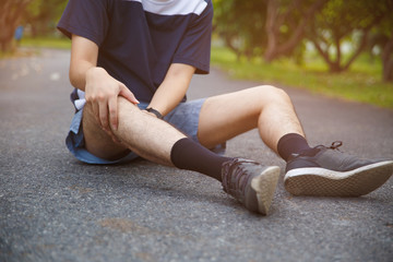 Male runner athlete knee injury and pain. Man suffering from painful knee while running in the public park.