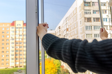 girl removes the mosquito net from the window in the autumn on a Sunny day
