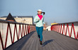 woman runnig on a wooden bridge, cardio exercise outdoors, taking care of her body, staying healthy and fit, in a white baseball hat, motion
