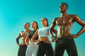 group of four young sportsmens women and men, fit athletes are standing on the sky background before