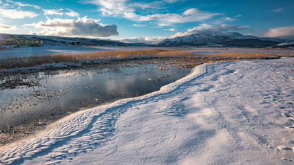 River flows through frozen field covered with snow