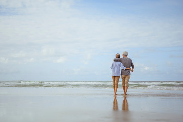 Wall Mural - Senior couples walking on the beach at sunny day, plan life insurance with the concept of happy retirement.