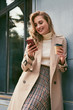 © Anton - Beautiful smiling blond girl in trench coat with coffee to go happily talking on cellphone outdoor