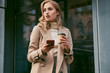 © Anton - Attractive casual blond girl in stylish trench coat with coffee to go and cellphone outdoor