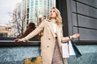 © Anton - Beautiful stylish blond girl in trench coat with shopping bags confidently looking away on street