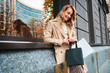 © Anton - Portrait of pretty joyful blond girl in beige coat with shopping bags on street