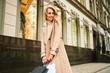 © Anton - Pretty smiling stylish blond girl in beige coat with shopping bags joyfully looking away on street