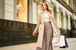 © Anton - Pretty stylish blond girl in beige coat with shopping bags walking on street