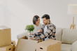 © VK Studio - Happy couple in love settle in new home, unpack boxes with household objects, man holds potted plant, woman embraces and expresses love to husband, start new family life in modern apartment.