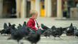 © MEDIAIMAG - Baby child sitting on the ground and feeding pigeons, boy rising up, birds fly