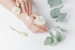 © Parilov - Woman applying hand cream flowers eucalyptus on white background, top view. Concept cosmetic body care, anti-wrinkles, anti-aging spa