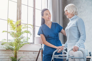 young female social worker helping senior woman to walk with walker at home