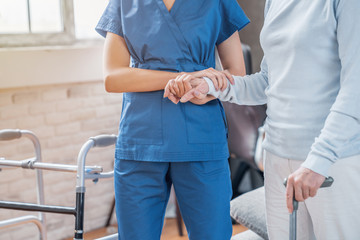 Cropped of female social worker helping senior woman to walk with walker at home