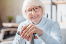 Senior Woman Holding Cane While Sitting On Sofa At Home With Focus On Hands. Old People Healthcare Concept