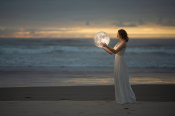 Wall Mural - astrology. secret and riddle. beautiful attractive girl on a night beach with sand hugs the moon, ar