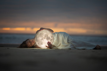 astrology. secret and riddle. beautiful attractive girl on a night beach with sand hugs the moon, ar
