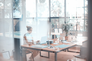 Abstract photo of a woman working on her laptop, taken through the glass