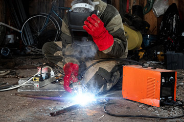 A male welder in a welding mask works with an arc electrode in his garage. Welding, construction, metal work.