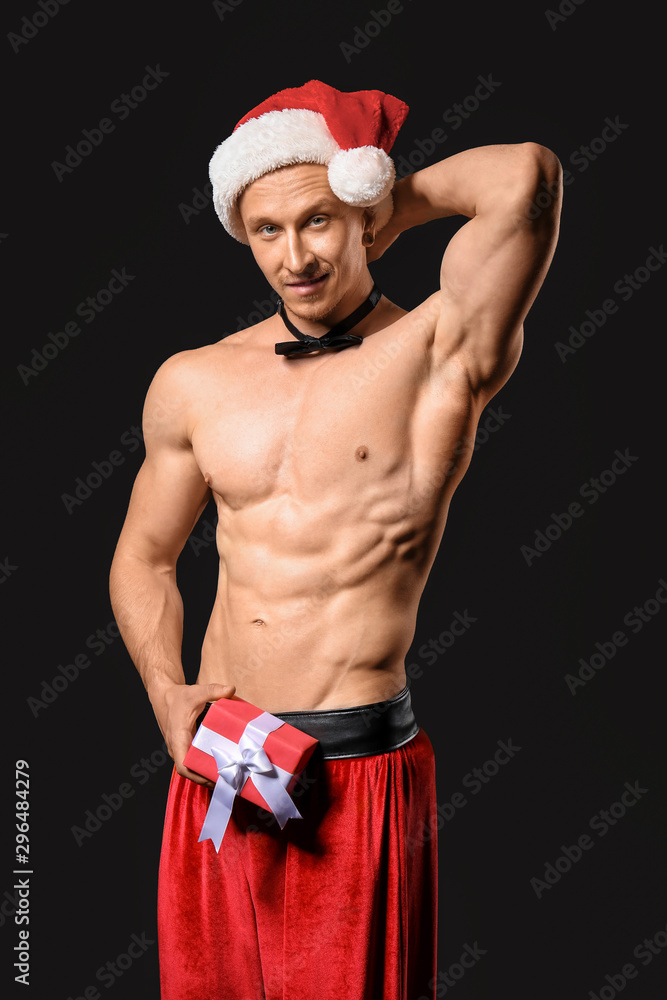 Young athletic Santa Claus with gift on dark background