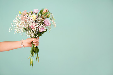 female hand with bouquet of beautiful flowers on color background