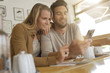 © goodluz - Young couple looking at a cell phone in a coffee shop