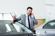 © zorandim75 - Businessman talking on phone near car in modern dealership.