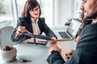 © HBS - Mature female estate agent showing terms of agreement in contract to young family couple sitting at the desk in bright office. Dealership, home purchasing, signing a contract concept