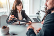 © HBS - Mature female estate agent showing terms of agreement in contract to young family couple sitting at the desk in bright office. Dealership, home purchasing, signing a contract concept