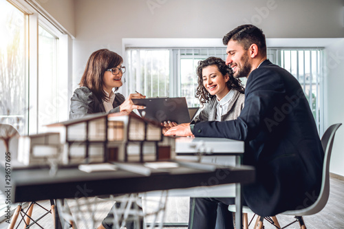 Side view of young happy family sitting in consulting office, making property purchase. Female realtor helping business couple do financial investment. Installment payment, mortgage, loan concept