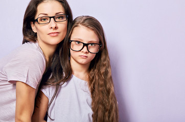 Wall Mural - Happy young casual mother and serious sad kid in fashion glasses hugging on purple background with empty copy space.