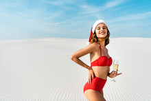 Sexy And Smiling Woman In Santa Hat And Swimsuit Holding Champagne Glass On Beach In Maldives