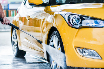 Man cleaning vehicle with high pressure water jet. Car wash details or close up.