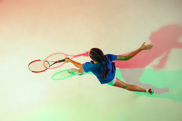 Wall Mural - Young woman in blue shirt playing tennis. She hits the ball with a racket. Indoor studio shot with mixed light. Youth, flexibility, power and energy. Top view.