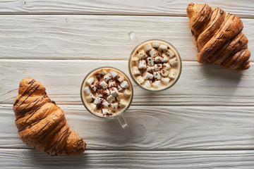 top view of cacao with marshmallow near cookies and croissants on white wooden table