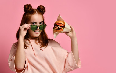 Beautiful teenage girl with red hair holding burger and beverage in hand. Ginger student girl has fast food lunch