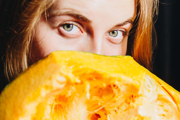 girl with long blond hair playfully looks holding a pumpkin in her hands. concept photo for halloween. on a black background