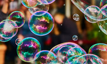 Metallic Glowing Colorful Soap Bubble In The Air In Front Of A Blurry Abstract Background