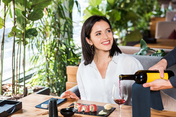 Wall Mural - cropped view of waiter pouring red wine in glass near attractive woman