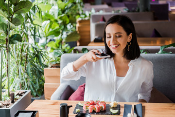 Wall Mural - happy woman taking photo of tasty sushi in restaurant