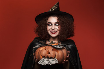 Image of witch girl in halloween costume holding pumpkin with money