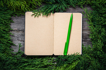 Wall Mural - Christmas frame from fir branches on a background of an old gray board around an open notebook with blank sheets. Frame of fir branches. Christmas card blank concept.