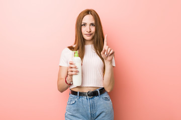 Wall Mural - Young caucasian woman holding a cream bottle showing number one with finger.