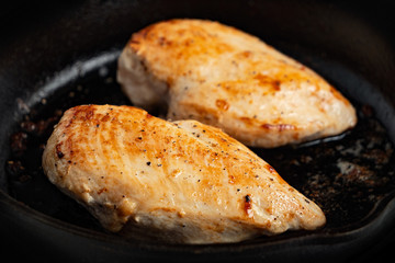 Closeup of two whole chicken breasts roasting in cast iron pan.