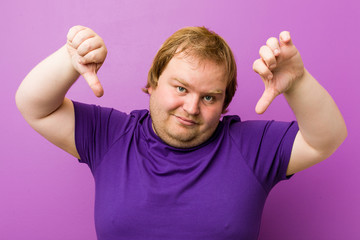 Wall Mural - Young authentic redhead fat man showing thumb down and expressing dislike.