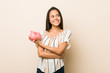 © Asier - Young hispanic woman holding a piggy bank smiling confident with crossed arms.