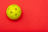 Fototapeta Dziecięca - Bright yellow pickleball or whiffle ball on a solid bright red flat lay background symbolizing sports and activity with copy space.